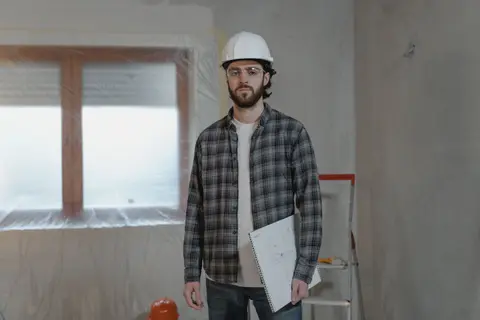 Adult male construction worker holding blueprints in an indoor renovation site.