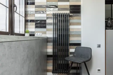Stylish home interior featuring a tiled wall, radiator, and designer chair.
