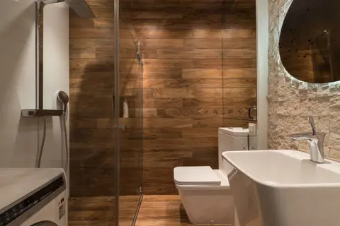 Stylish modern bathroom interior design with glass shower enclosure toilet bowl and sink under oval mirror