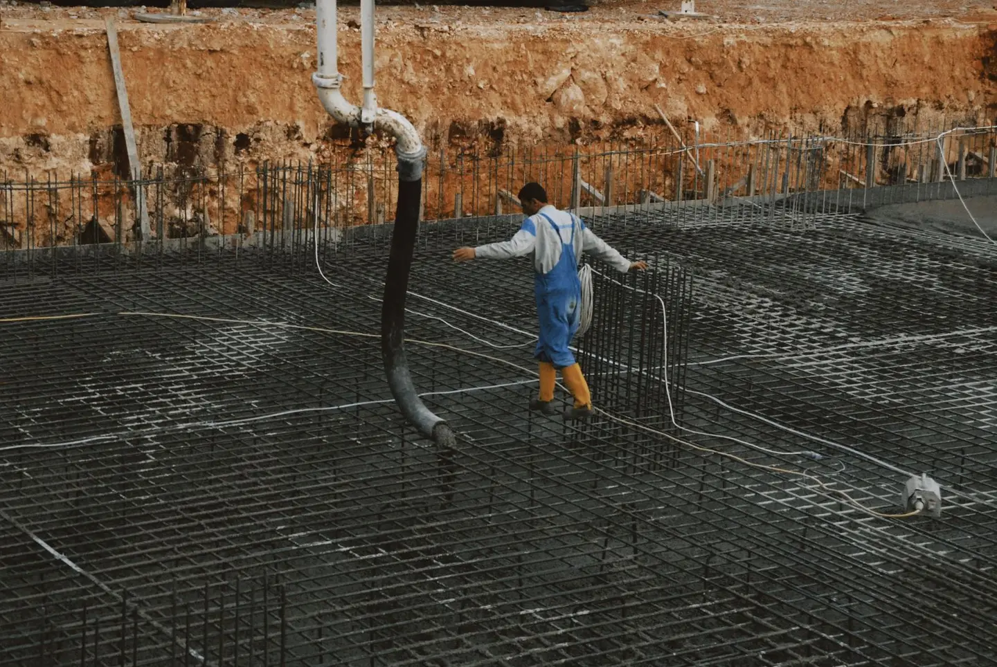 A construction worker in yellow boots walks on rebar grid at a building site.