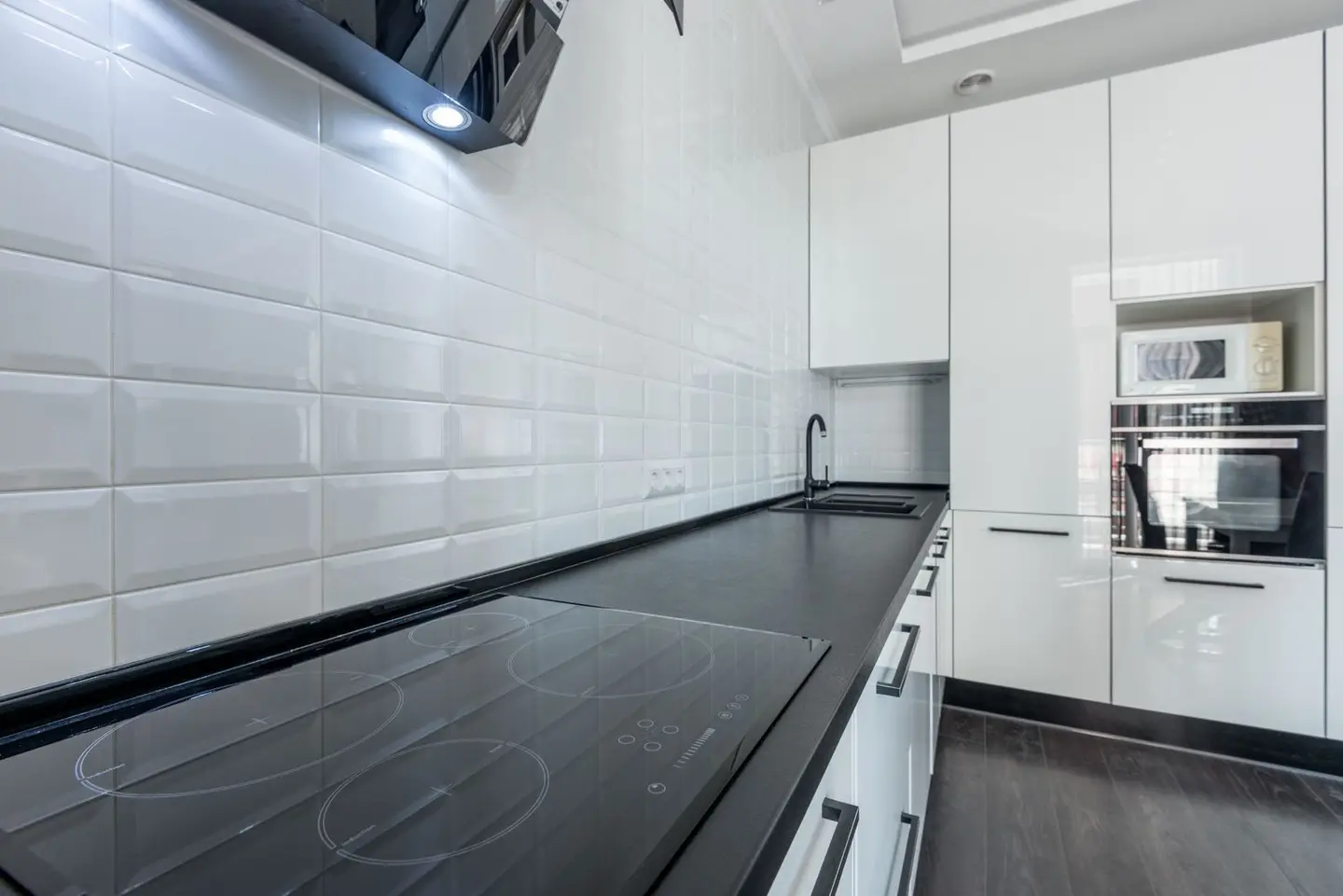 Interior of modern light white kitchen furnished with white cupboards and appliances with wooden floor and tiled wall