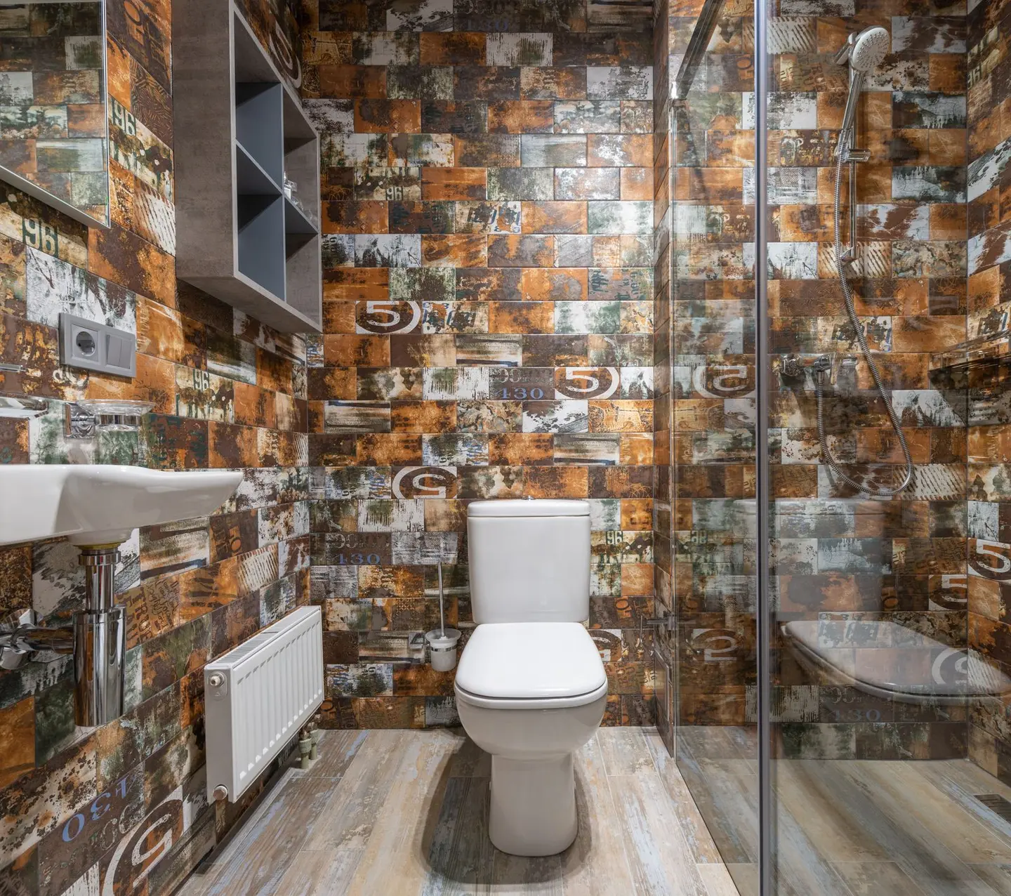 White ceramic toilet placed at wall near glass door of modern shower cabin in light bathroom with shelves and radiator