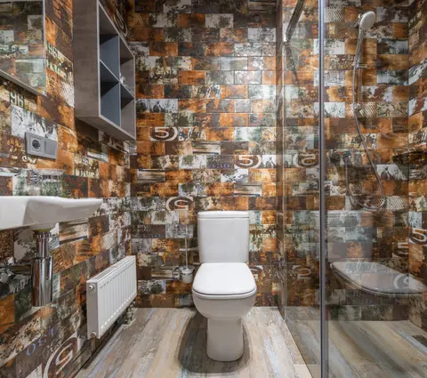 White ceramic toilet placed at wall near glass door of modern shower cabin in light bathroom with shelves and radiator