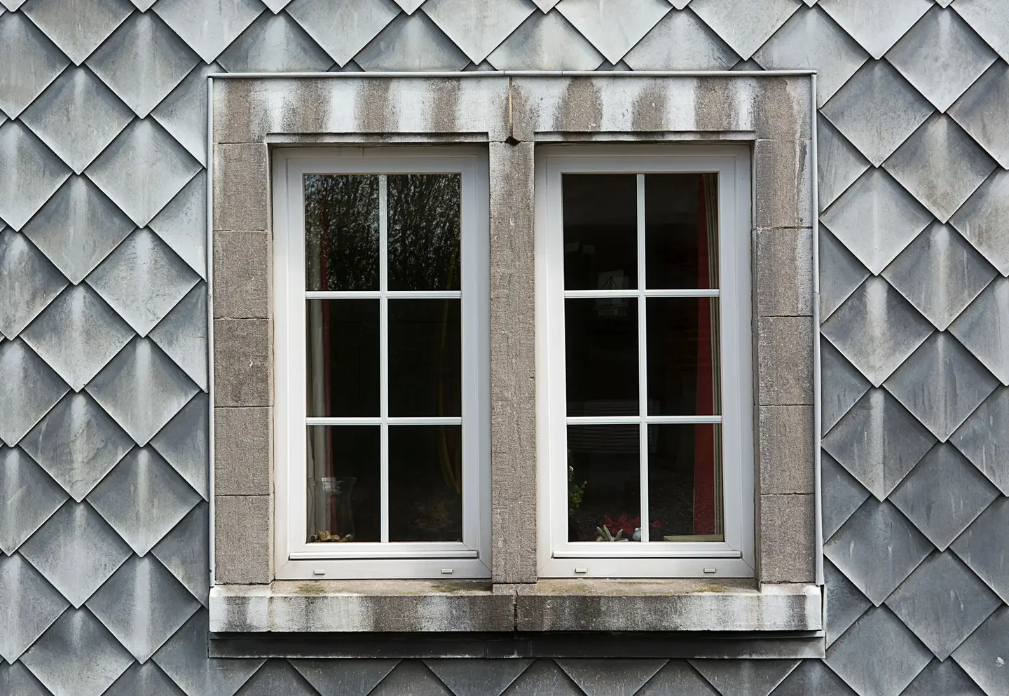 Closeup of a modern double window set in a textured shingle facade, highlighting architectural details.