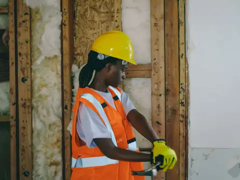 Female construction worker in PPE hammering indoors on a renovation site.