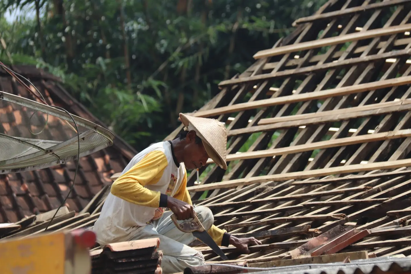 Carpenter working on a wooden roof structure outdoors in a rural setting with traditional tools.
