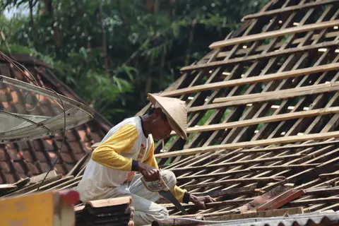 Carpenter working on a wooden roof structure outdoors in a rural setting with traditional tools.