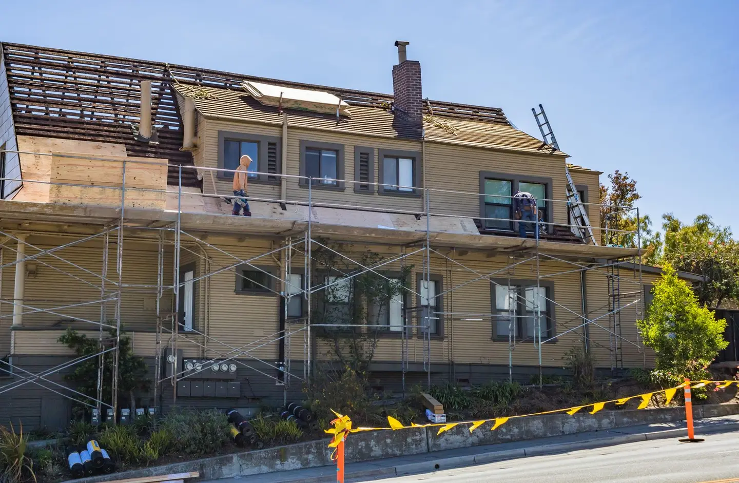 A house under renovation with scaffolding up and roofers working on the roof covering.