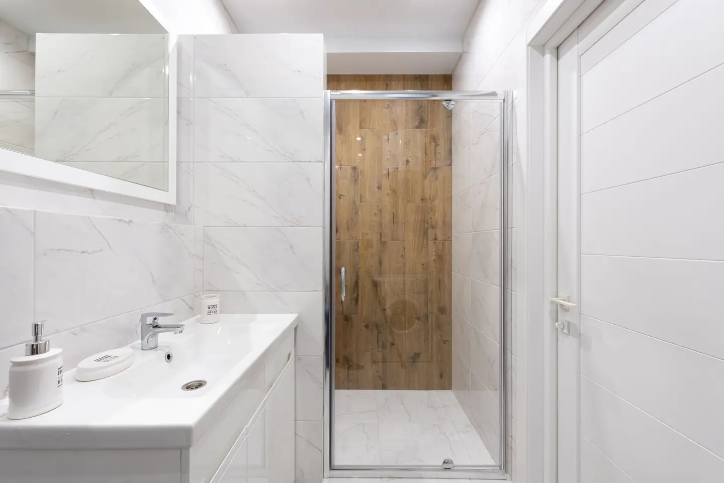 Modern bathroom with washstand under rectangular mirror on tiled wall against shower room in light house