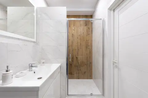 Modern bathroom with washstand under rectangular mirror on tiled wall against shower room in light house