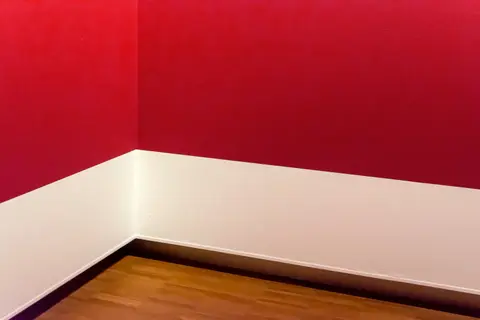 A minimalist room corner with striking red walls and wooden flooring, showcasing modern design.