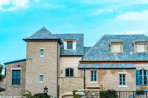 A picturesque stone house featuring a slate roof and blue shutters against a vibrant sky.
