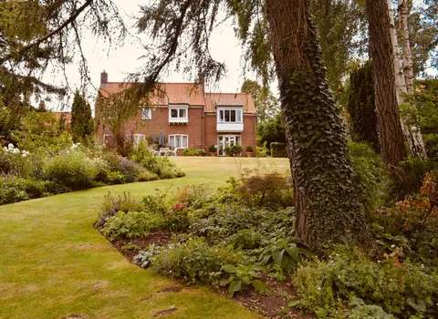A classic English-style brick house surrounded by a lush, verdant garden.