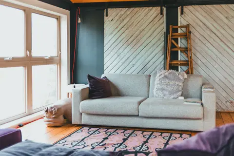 Bright and cozy modern living room featuring a comfortable sofa, wooden ladder, and large windows.
