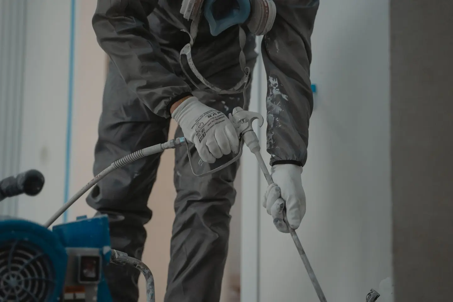 Worker in protective gear using a power spray for indoor renovation.