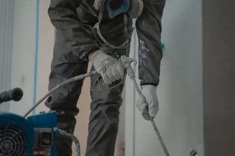 Worker in protective gear using a power spray for indoor renovation.