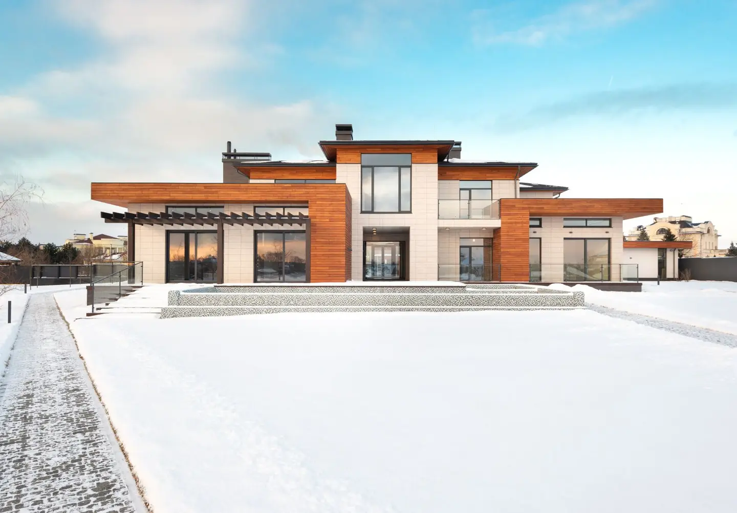 Exterior design of modern cottage house facade with large windows and mixed wooden and stone cladding and spacious yard in snowy winter suburban area