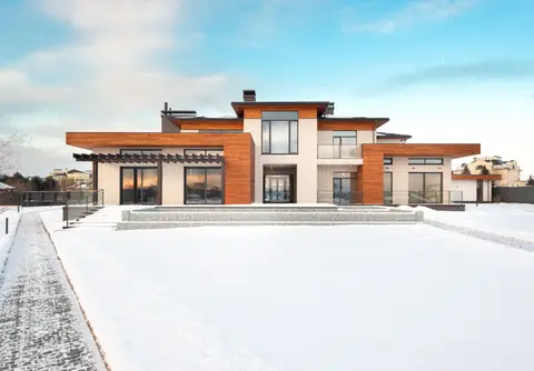 Exterior design of modern cottage house facade with large windows and mixed wooden and stone cladding and spacious yard in snowy winter suburban area