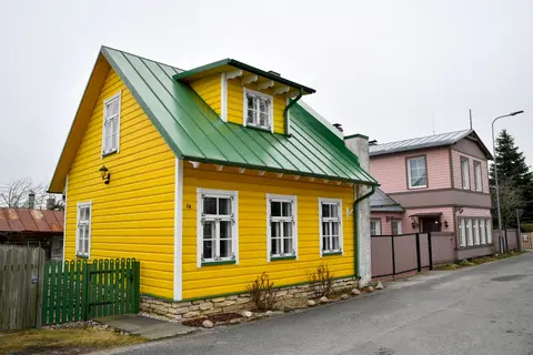Beautiful yellow wooden house with green roof in a picturesque Estonian neighborhood.