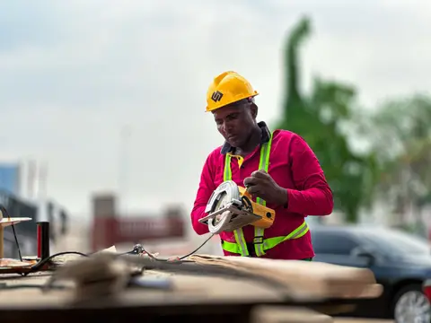 A construction worker in a hard hat operates a circular saw on a building site.