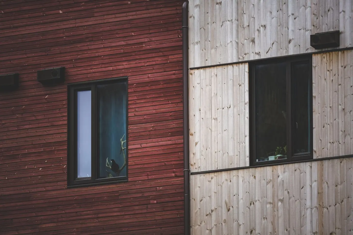 A close-up view of a red and beige wooden facade with modern windows, showcasing architectural contrast.