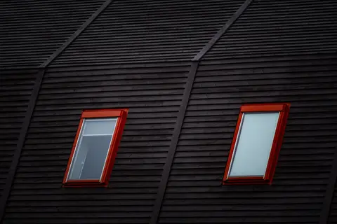 Close-up of a dark wooden roof featuring two red-framed windows adding a modern flair.