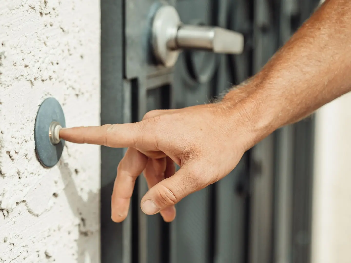 A close-up image of a hand pressing a doorbell outside a modern residential door.