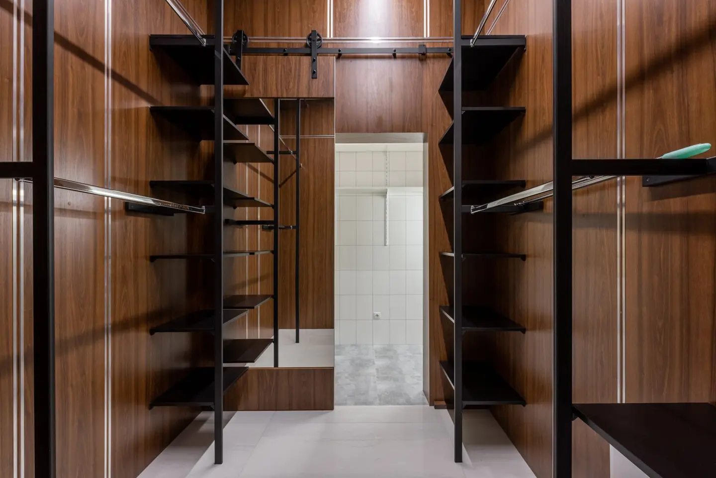Empty black shelves and racks placed in modern walk in wardrobe with brown walls and mirror with reflection at home